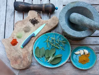 Spices, herbs, a knife and a mortar on a wooden kitchen table