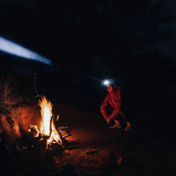 Camper wearing a headlamp next to a campfire at night