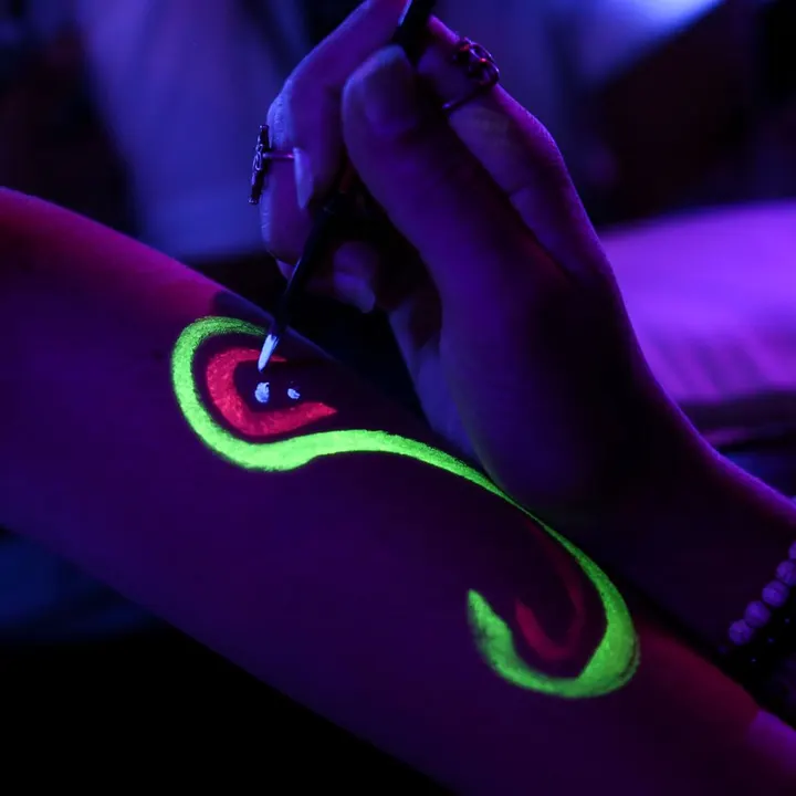 Neon UV body paint glowing on an arm under blacklight