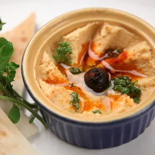 A bowl of hummus with olive oil, herbs and pita triangles
