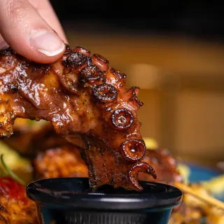 A grilled octopus tentacle dipped in a dark sauce, on a blue plate