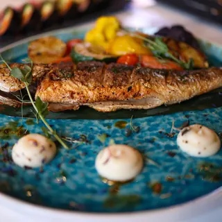A whole grilled fish on a blue plate with vegetables