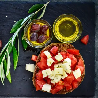 Tomato with cubes of feta on a barley rusk, olives and olive oil beside it