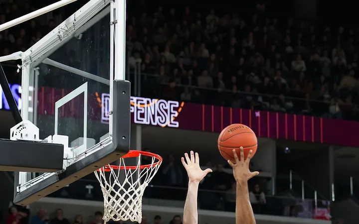A hand reaching for the ball above the rim during an indoor basketball game