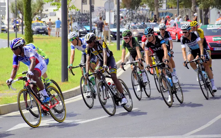 A group of road cyclists racing through a town, spectators along the road