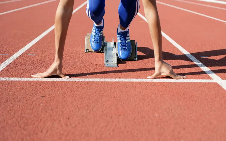 A sprinter's hands and spikes on the starting line of a red running track