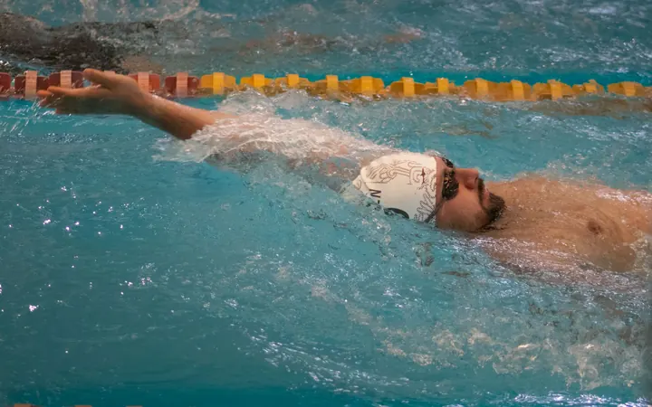 A swimmer in a white cap doing backstroke in a racing lane