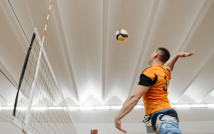 A volleyball player in an orange shirt jumping to spike the ball in a sports hall