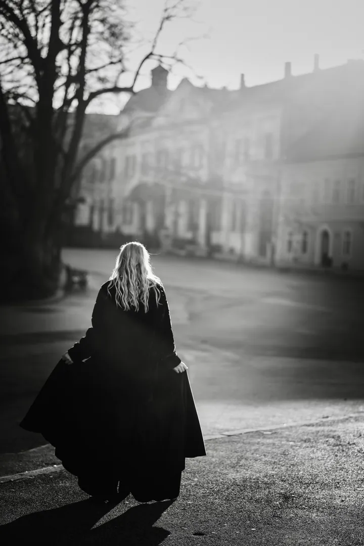 Black and white photo of a model in a long coat walking away down an old street