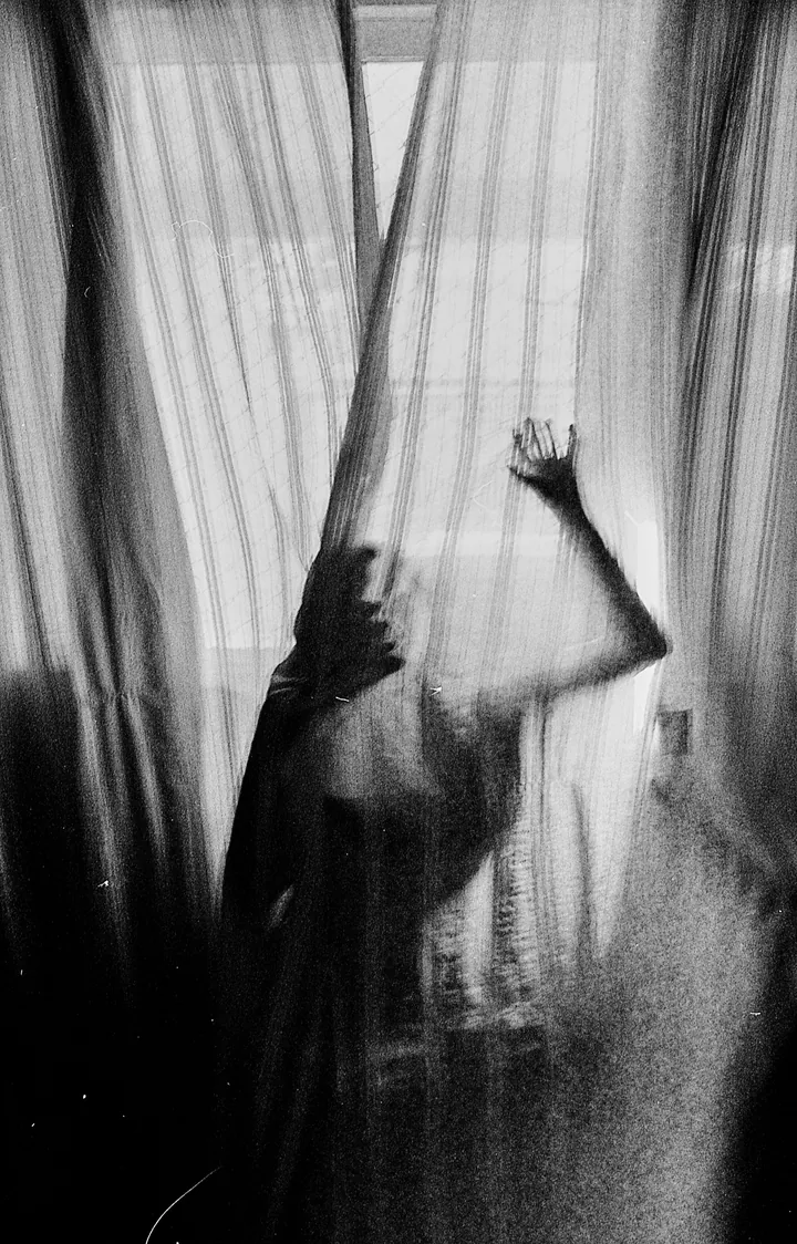 Black and white silhouette of a hand pressed against a sheer curtain
