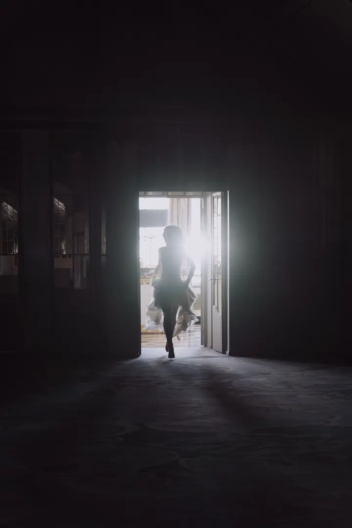 Silhouette of a model in a dress walking out through a bright doorway