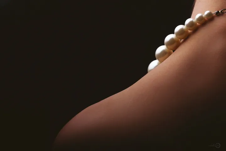 Pearl necklace on a bare shoulder against a dark background
