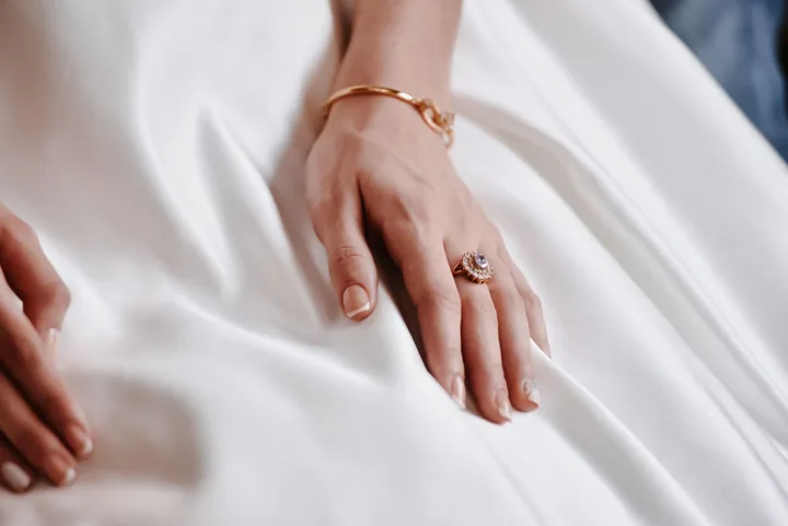 Hand with a ring and a fine bracelet resting on white satin