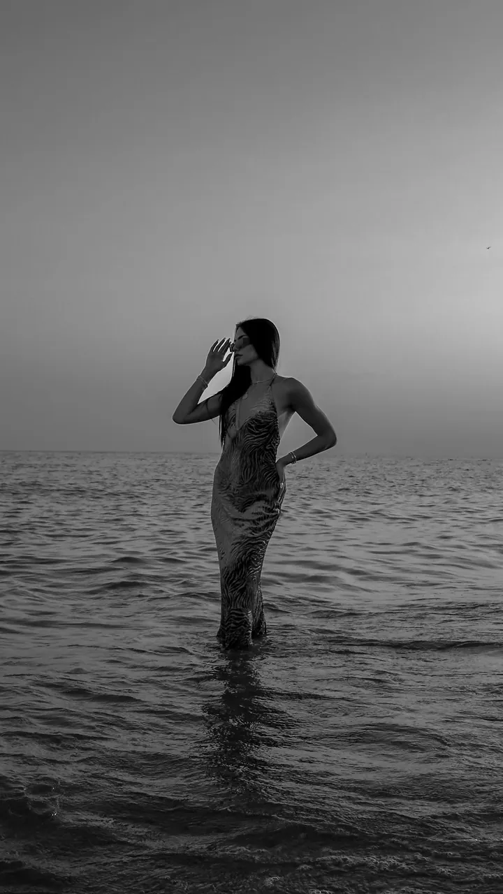 Black and white photo of a model standing in the sea at dusk
